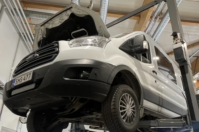 Pakettiauto nostimella konepelti avattuna huoltohallissa